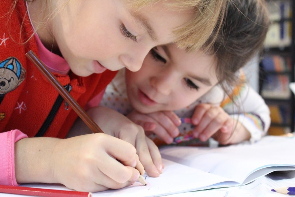 Two primary school age females crouched over a notebook drawing