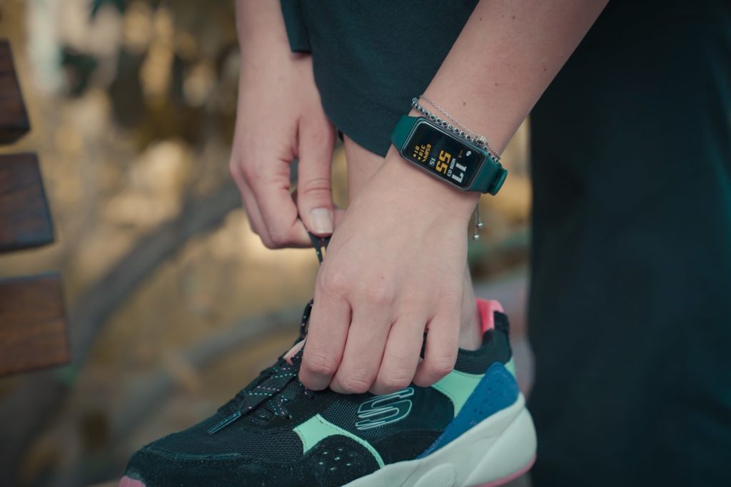 Someone doing up a shoelace and wearing a fitness tracker watch