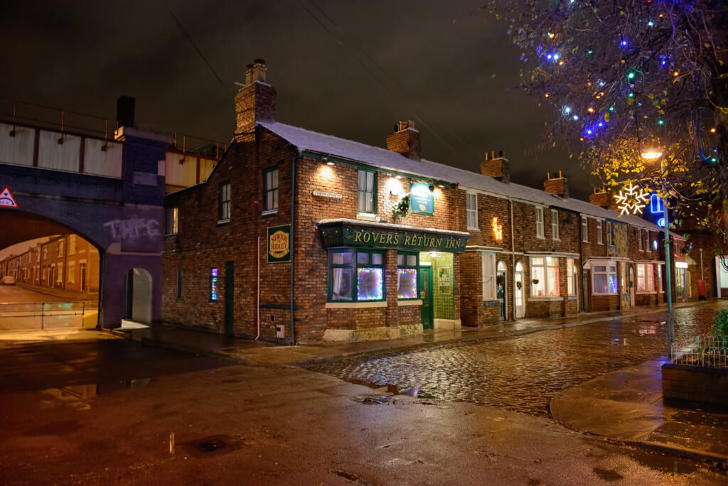 Coronation street with festive lights, in the foreground the Rovers Return Inn can be seen with festive decorations