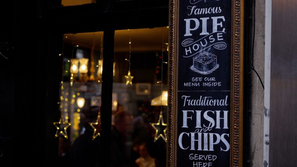 Blackboard advertises Pie and Mash and Fish and Chips, in background festive lights can be seen through the pub window. 